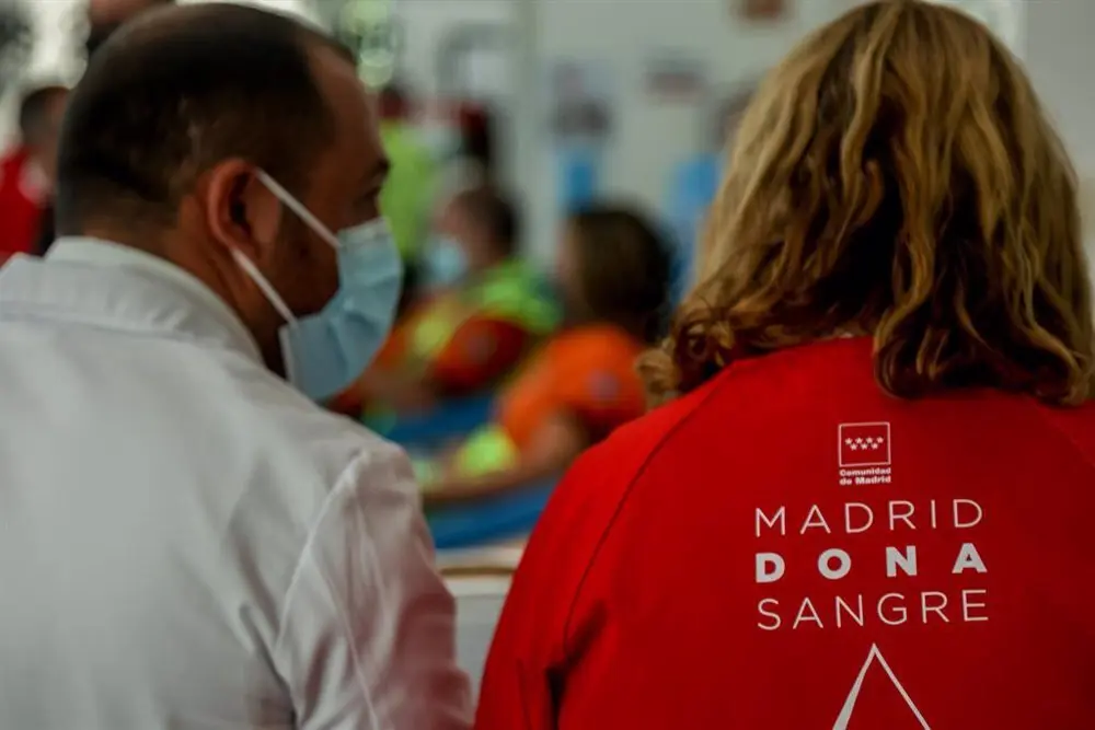 Hombre con mascarilla mirando a una mujer con una chaqueta roja en la que pone en su espalda "Madrid Dona Sangre"