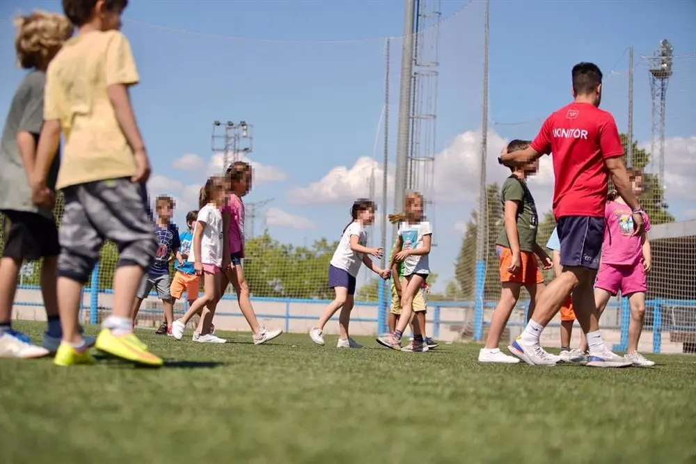 Ni&ntilde;os con un monitor de campamento en un campo de f&uacute;tbol
