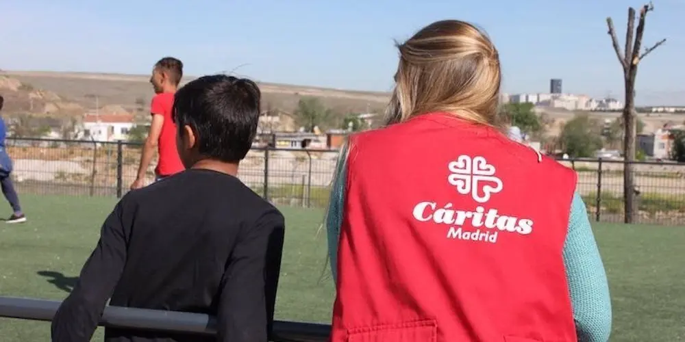Se&ntilde;ora con chaleco de C&aacute;ritas al lado de un ni&ntilde;o en un campo de f&uacute;tbol