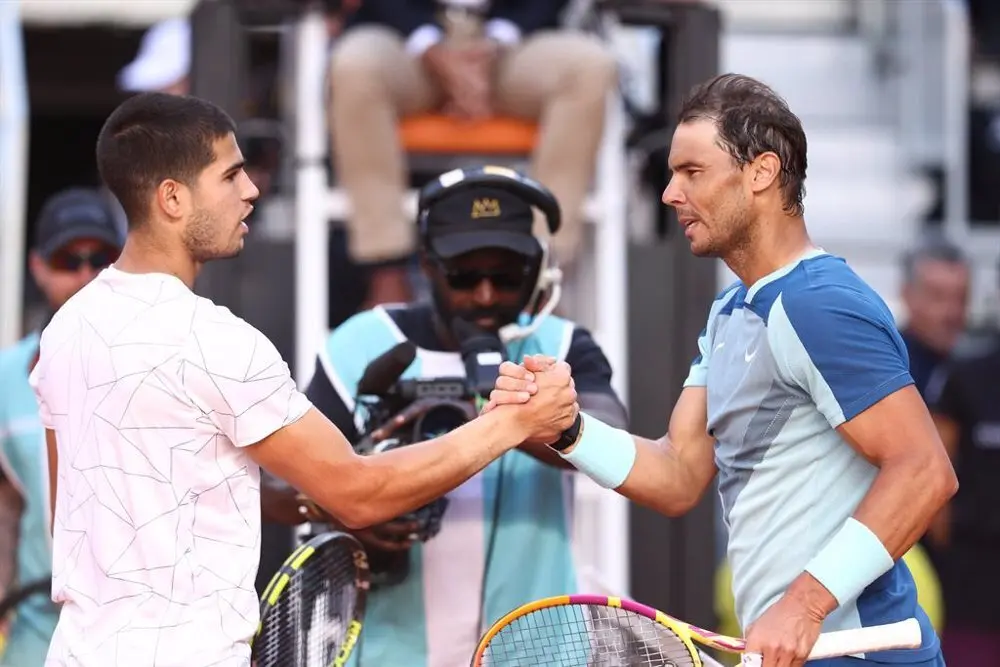 Alcaraz y Nadal d&aacute;ndose la mano en una pista de tenis