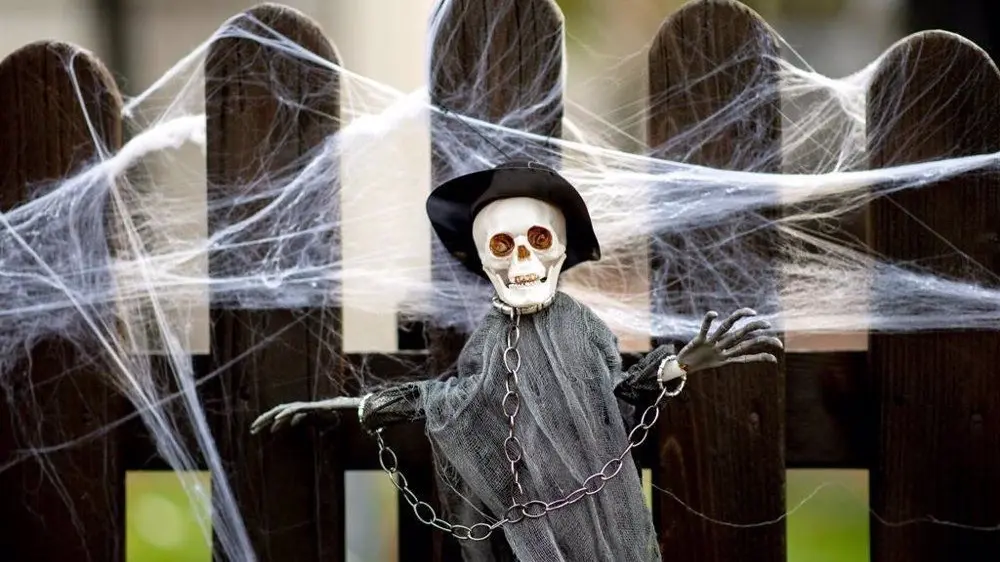 Mu&ntilde;eco de una calavera colgando de una valla rodeado de telara&ntilde;as