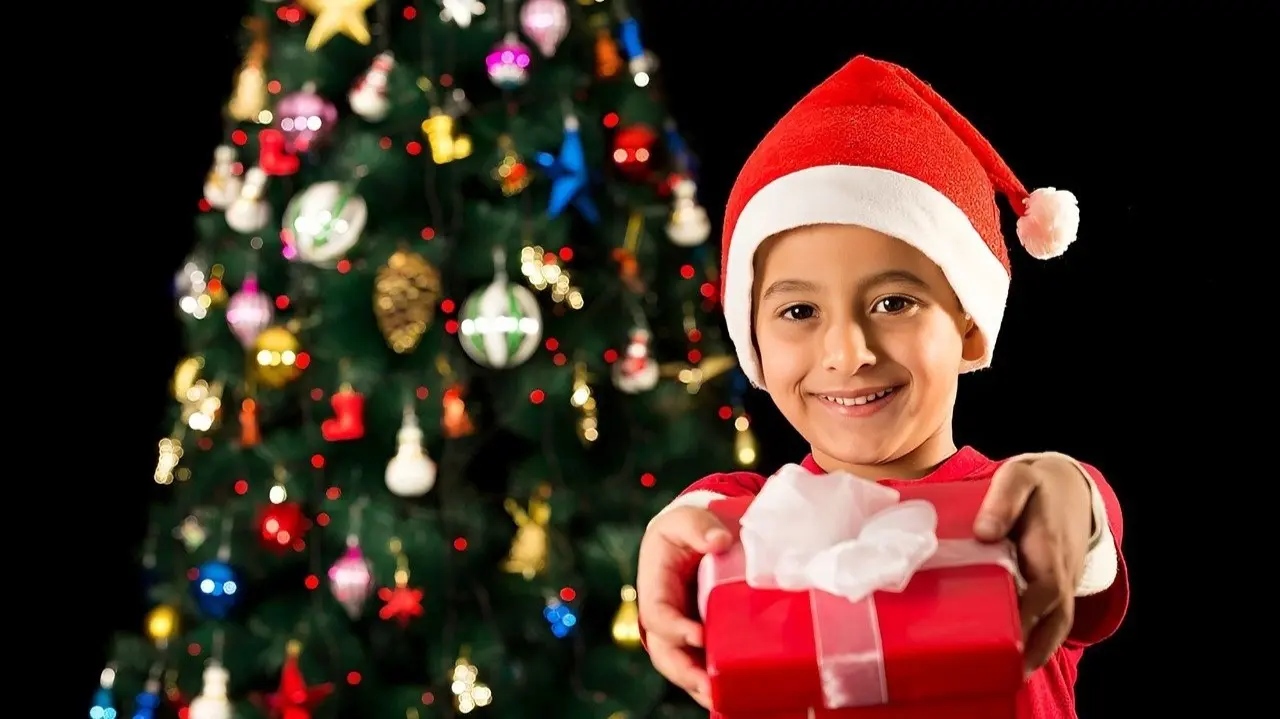 Ni&ntilde;o disfrazado de Pap&aacute; Noel ofreciendo un regalo.
