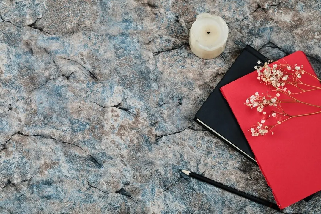 Cuadernos con flores, l&aacute;piz y vela sobre un fondo de m&aacute;rmol. Imagen de archivo.