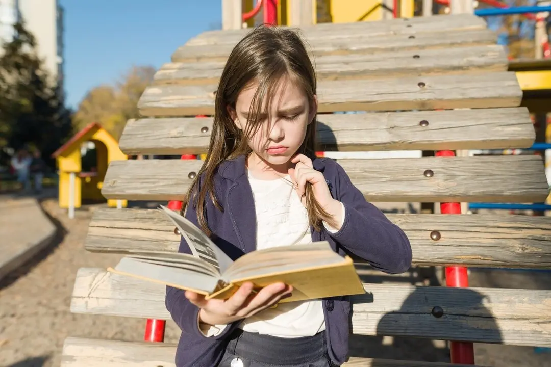 Ni&ntilde;a leyendo ofendida un libro en el parque. Imagen de archivo.