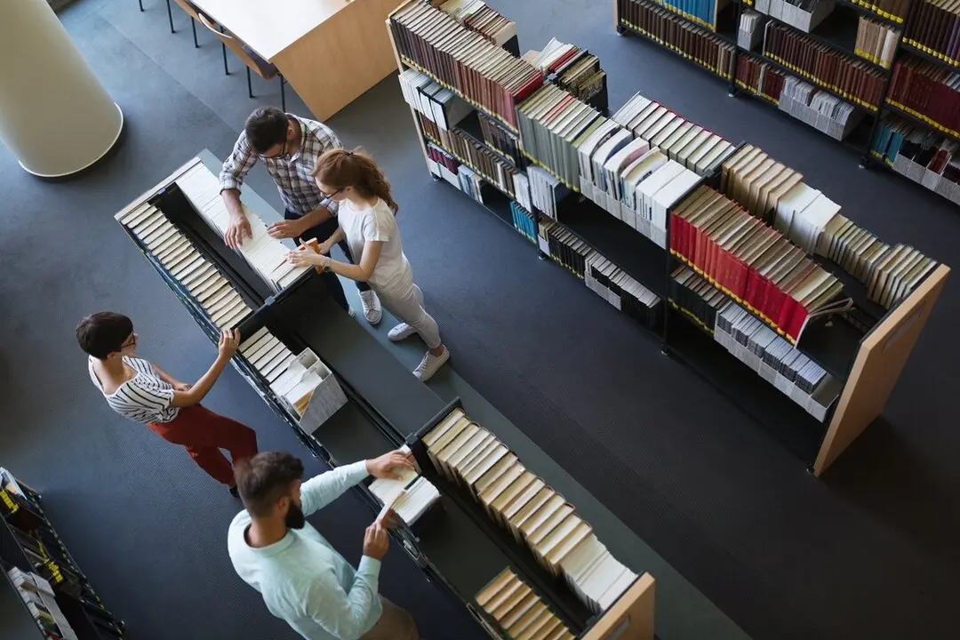 Grupo de personas buscando un libro en estanter&iacute;as. Imagen de archivo.