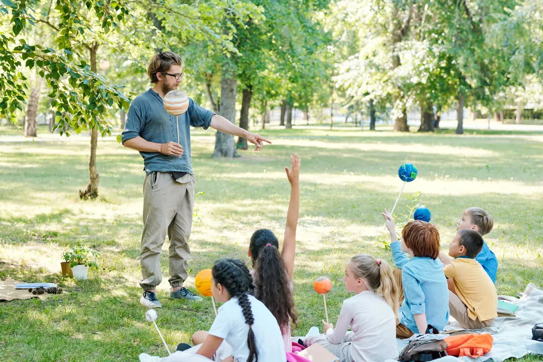 Ni&ntilde;os y ni&ntilde;as con un maestro en un parque. Imagen de archivo.