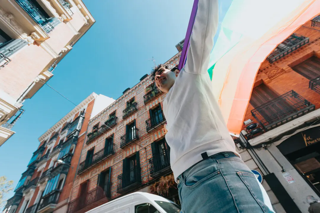 Joven con bandera lgtbi en la ciudad en un d&iacute;a de verano entre los edificios.