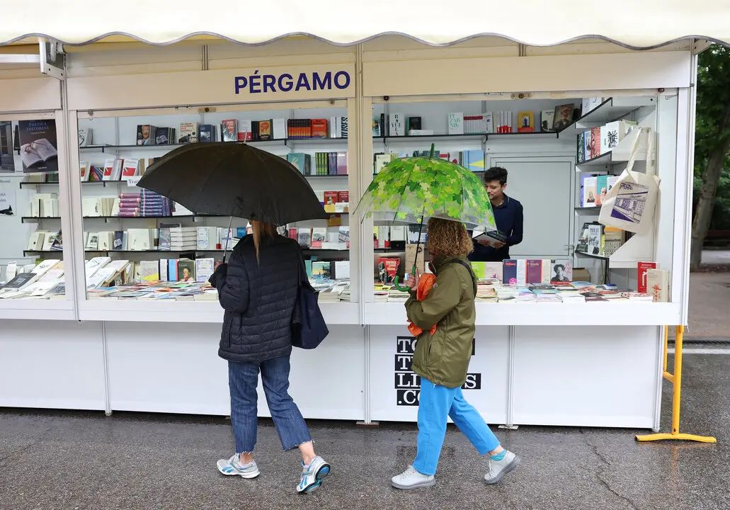 Visitantes bajo la lluvia en la caseta de la librer&iacute;a P&eacute;rgamo en la 82&ordf; #FLMadrid23 en el Retiro. 7 de junio de 2023. &copy; Isabel Infantes. Cedida por la Feria del Libro de Madrid.