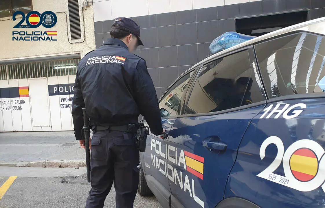 Un agente de la Polic&iacute;a Nacional frente a un coche patrulla.