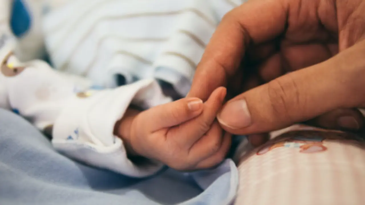 Mano adulta y mano de beb&eacute; entrelaz&aacute;ndose