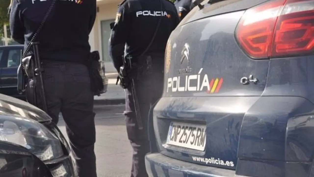 Coche de la Polic&iacute;a Nacional con dos agentes situados en frente de ellos de espaldas
