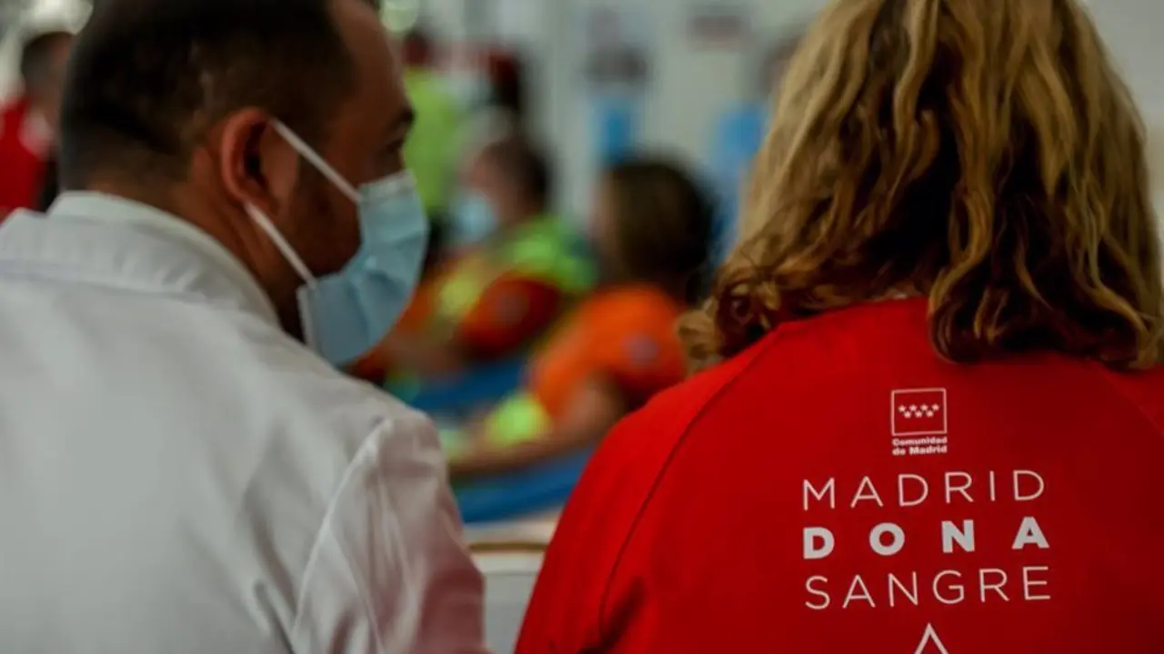 Hombre con mascarilla mirando a una mujer con una chaqueta roja en la que pone en su espalda "Madrid Dona Sangre"