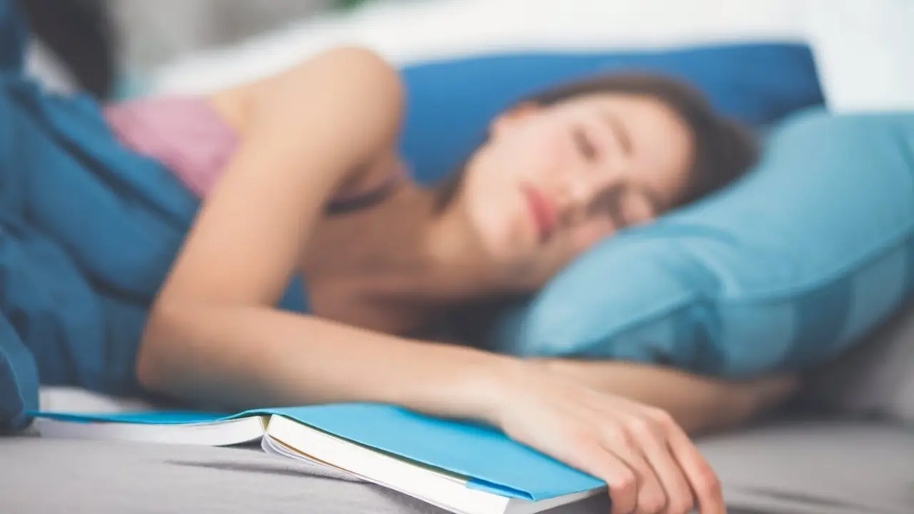 Mujer dormida en la cama despu&eacute;s de leer un libro