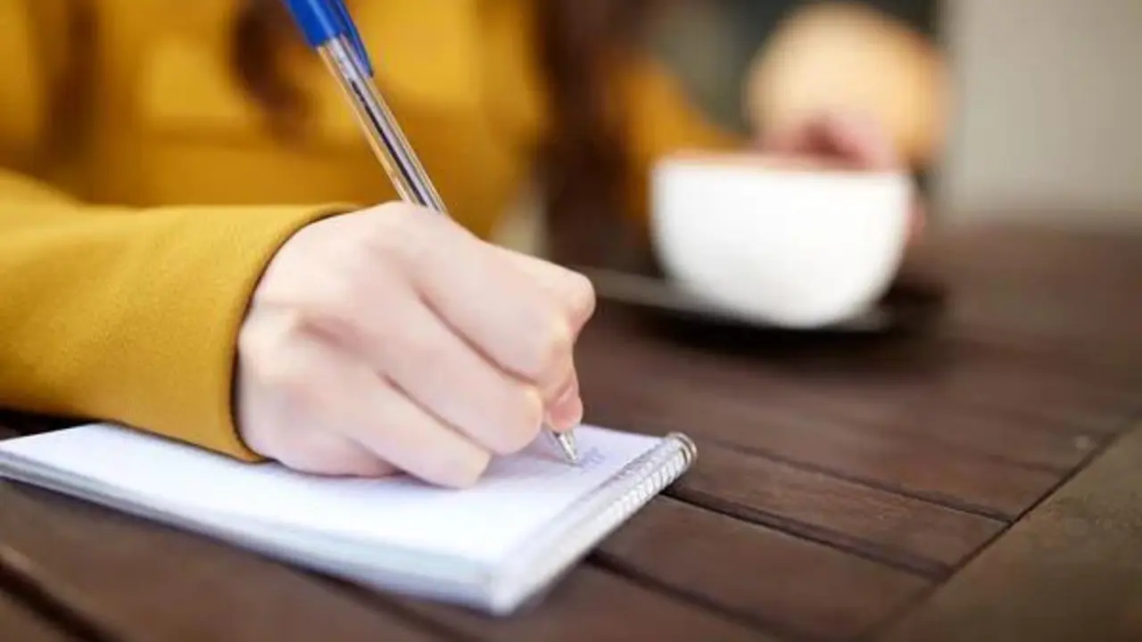 Persona escribiendo con una mano y con la otra sosteniendo una taza
