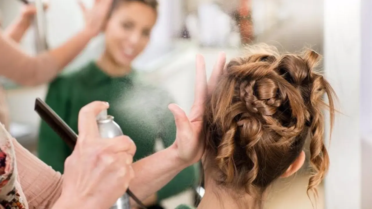 Persona echando laca en el pelo a otra para fijar el peinado