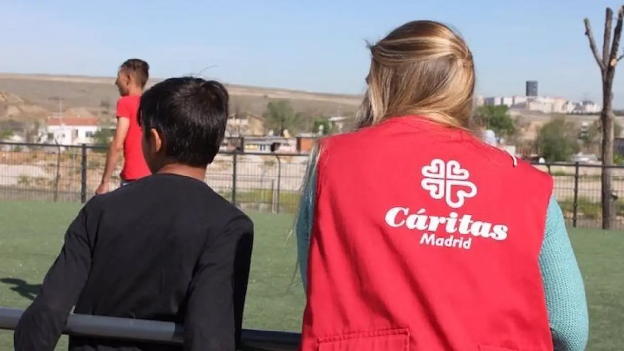 Se&ntilde;ora con chaleco de C&aacute;ritas al lado de un ni&ntilde;o en un campo de f&uacute;tbol