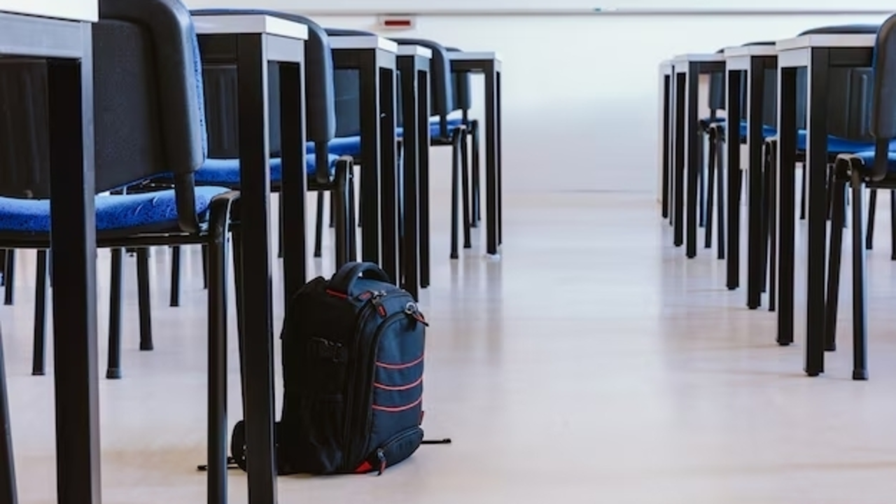 Mochila escolar en el suelo al lado de un pupitre en un aula vac&iacute;a