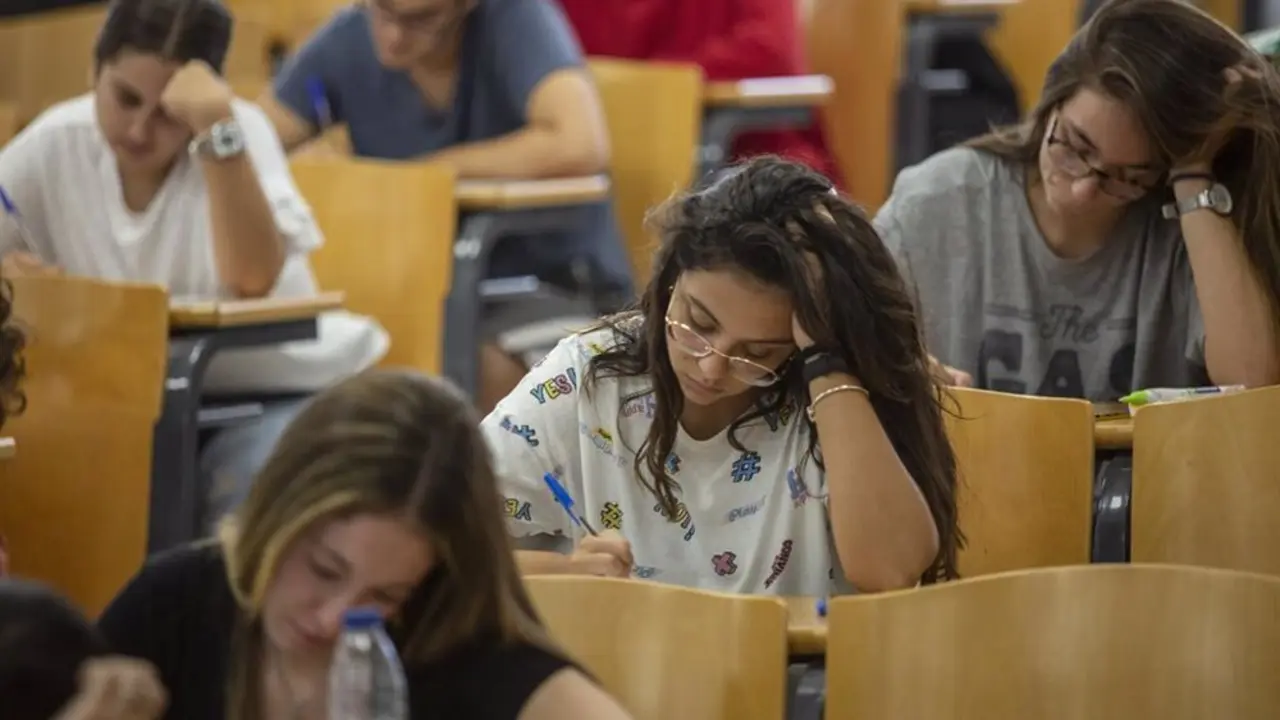 Personas sentadas en un aula con pupitres mir&aacute;ndolos