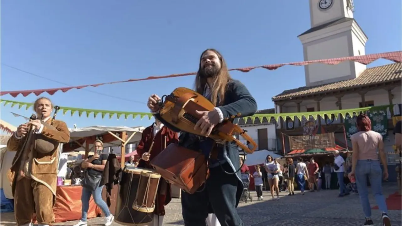 M&uacute;sicos con trajes medievales tocando diferentes instrumentos de la &eacute;poca en una plaza de pueblo 