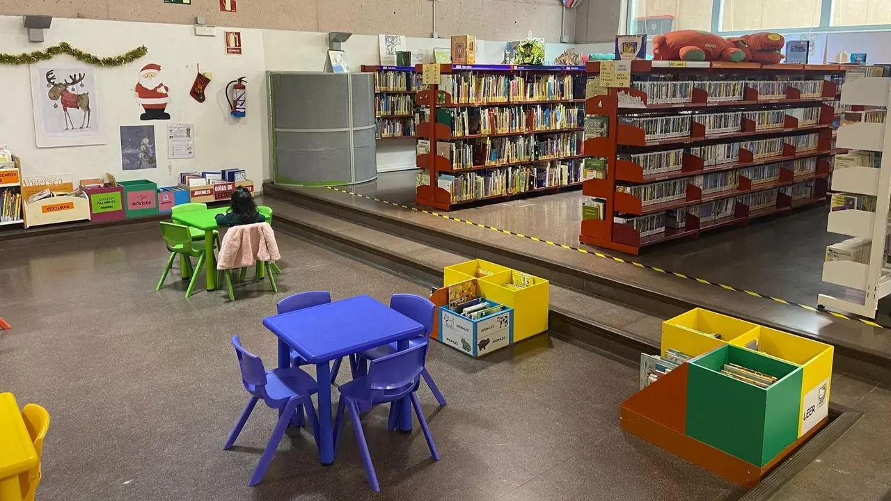 Sala de biblioteca infantil con estanter&iacute;as llenas de libros y mesas de colores