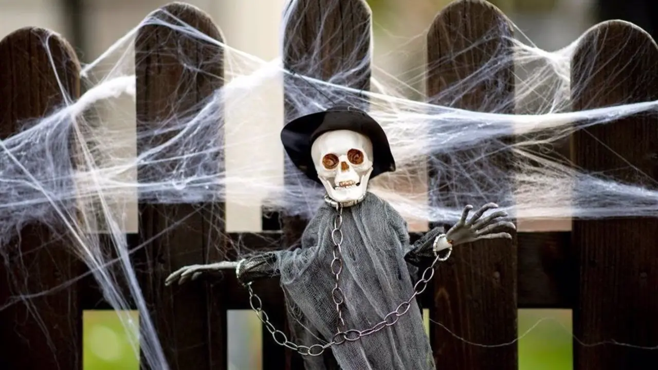 Mu&ntilde;eco de una calavera colgando de una valla rodeado de telara&ntilde;as