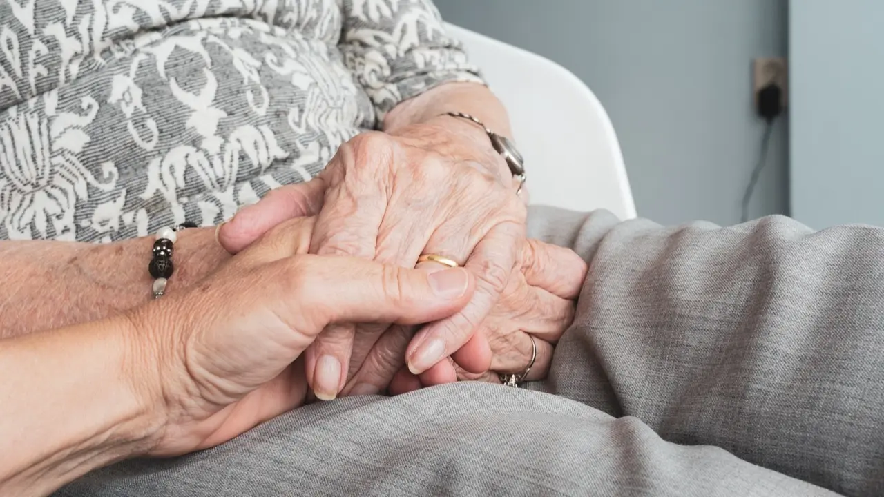 Manos de una persona mayor entrelazadas con las de una persona m&aacute;s j&oacute;ven