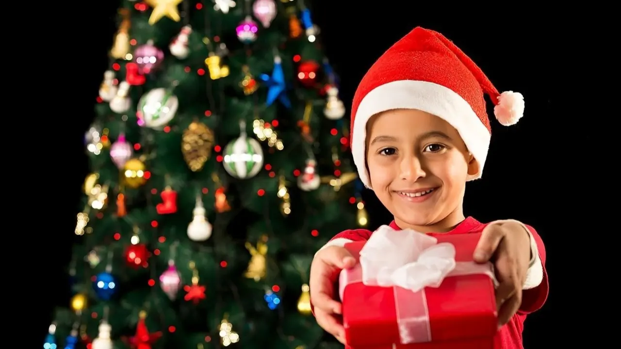 Ni&ntilde;o disfrazado de Pap&aacute; Noel ofreciendo un regalo.