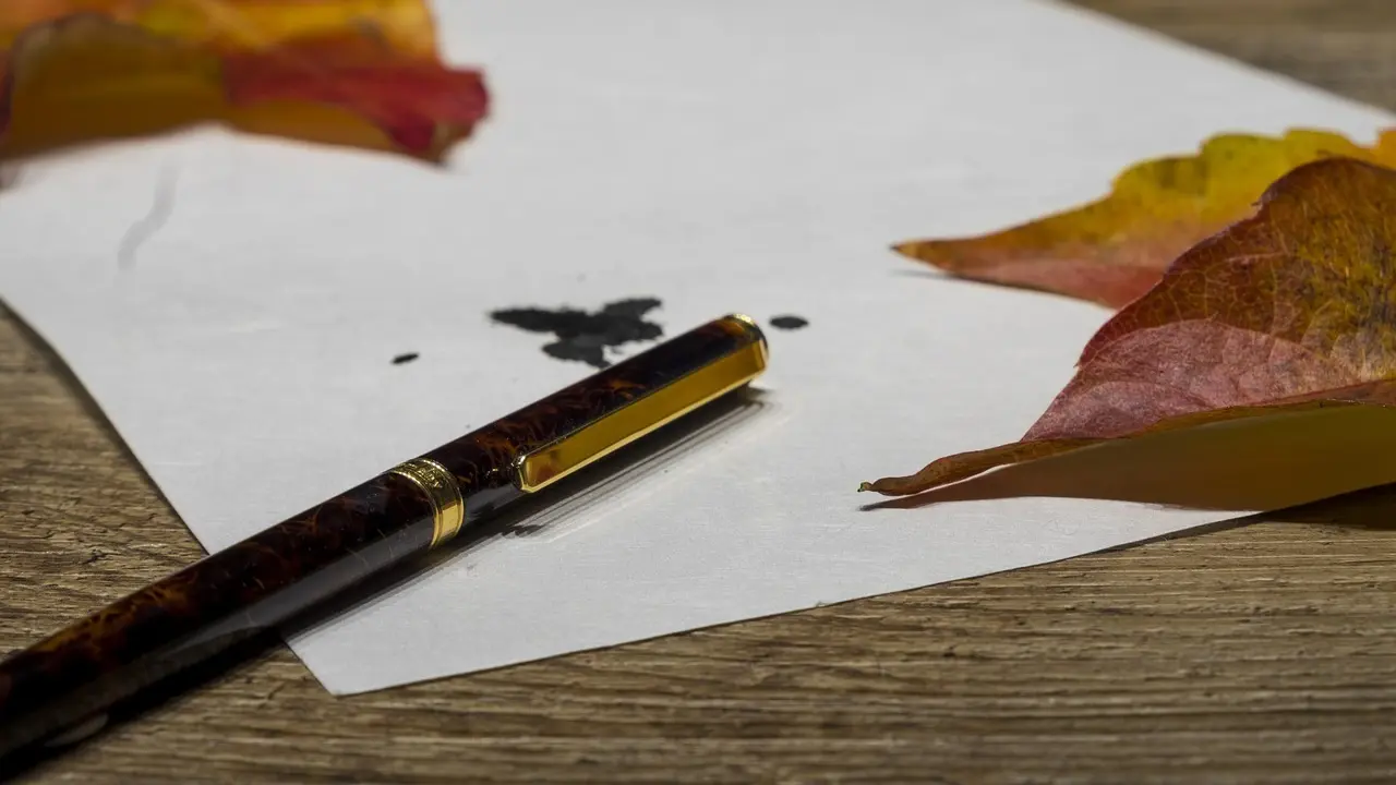 Pluma de tinta junto a una hoja en blanco.