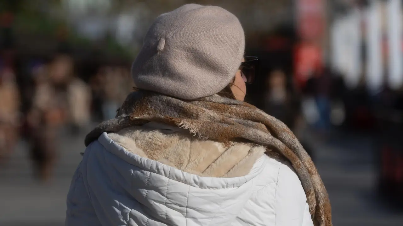 Mujer abrigada con abrigo, gorro y bufanda paseando por Madrid.
