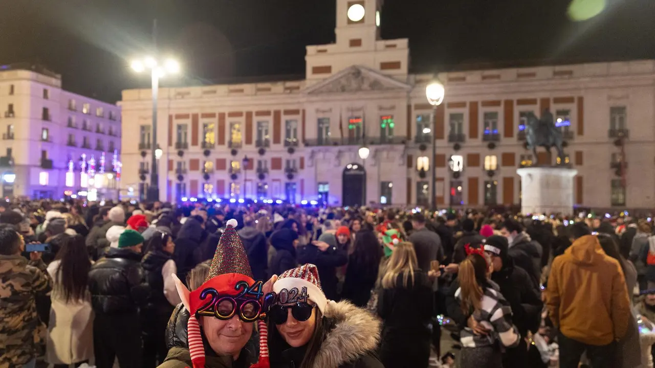Imagen de archivo. Dos personas disfrazadas se hacen una foto con el reloj de fondo, antes de las campanadas de Nochevieja 2023, en la Puerta del Sol.