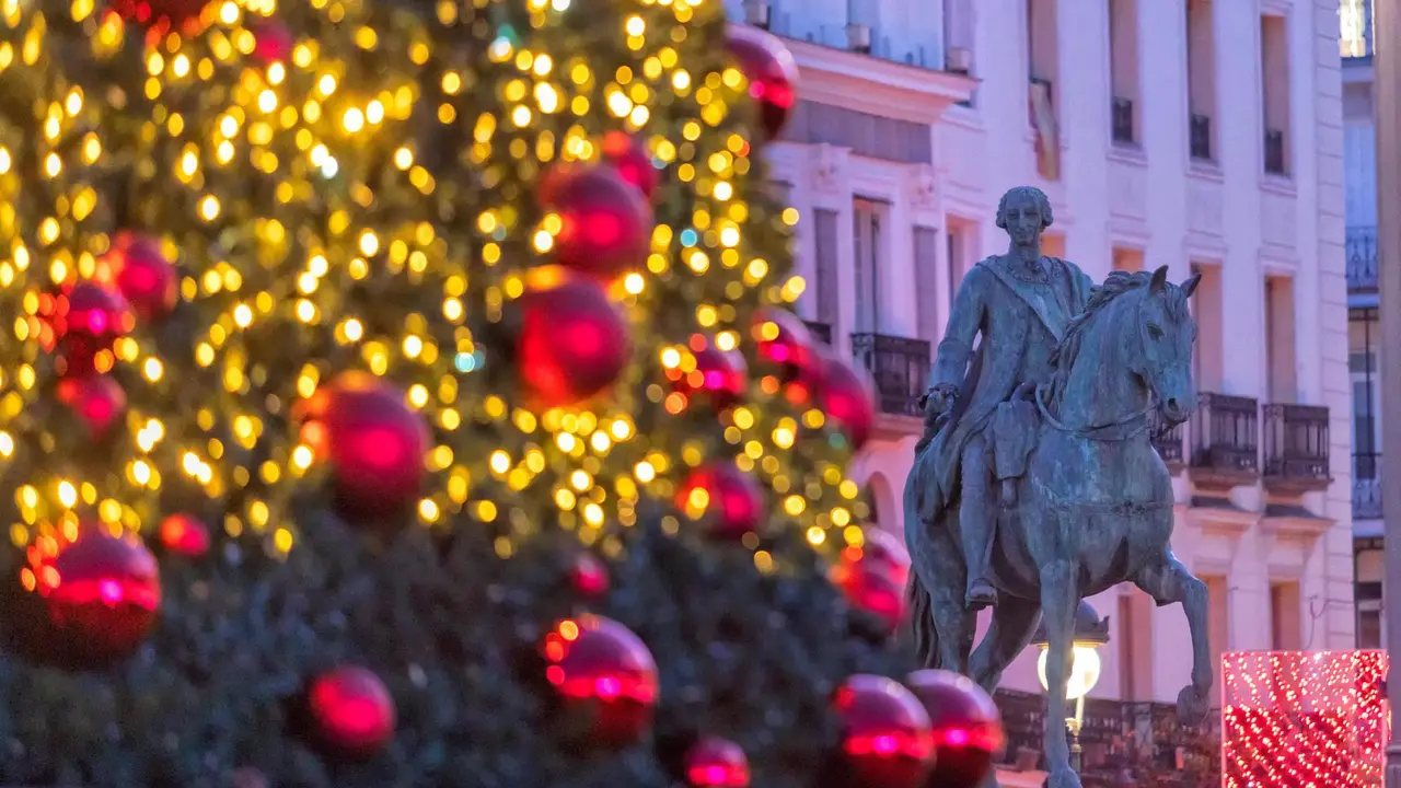 Detalle del &aacute;rbol de Navidad de la Puerta del Sol en primer plano desenfocado; tras &eacute;l, la estatua ecuestre de Carlos III. &Aacute;lvaro L&oacute;pez del Cerro &copy; Madrid Destino