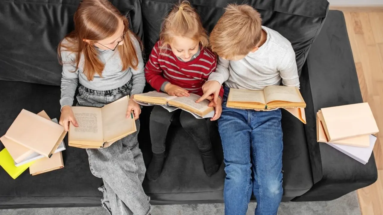 Tres ni&ntilde;os leen libros sentados en el sof&aacute;. Imagen de archivo.