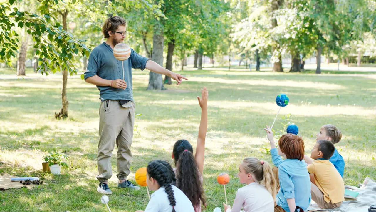 Ni&ntilde;os y ni&ntilde;as con un maestro en un parque. Imagen de archivo.