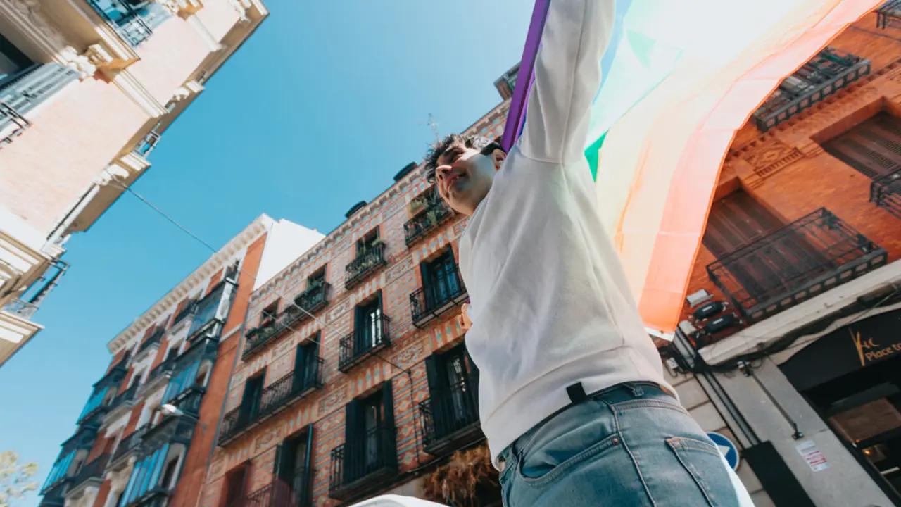 Joven con bandera lgtbi en la ciudad en un d&iacute;a de verano entre los edificios.